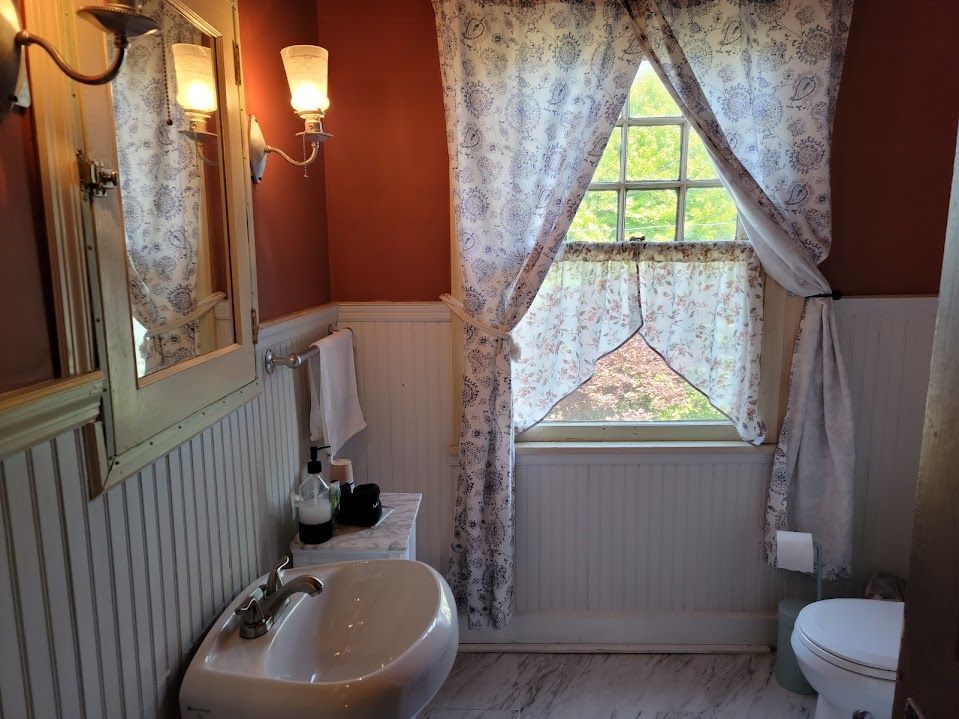 Bathroom with white beadboard, red-orange wall, floral curtains, sink, and toilet.
