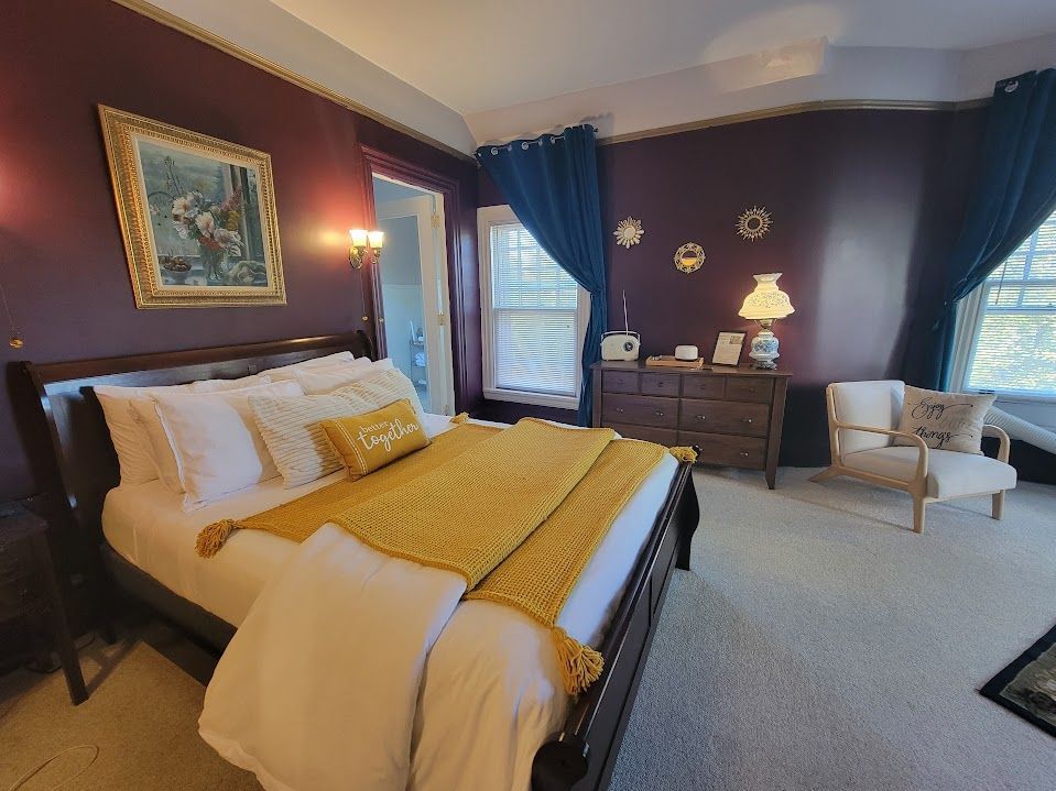 Bedroom with maroon walls, bed with yellow blanket, white pillows, and dresser.