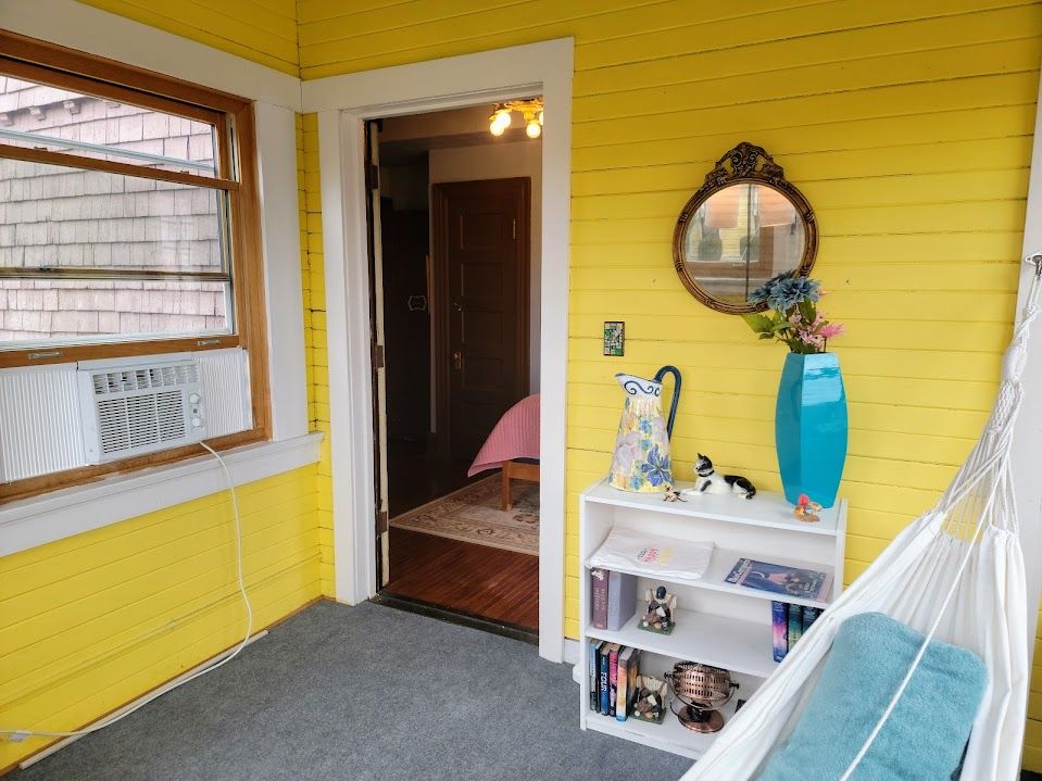 Yellow porch with open doorway, window, bookcase, mirror, and hammock.