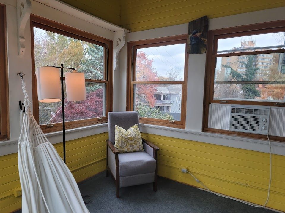Sunroom with yellow walls, windows, a chair, hammock, and floor lamp. Autumn foliage outside.
