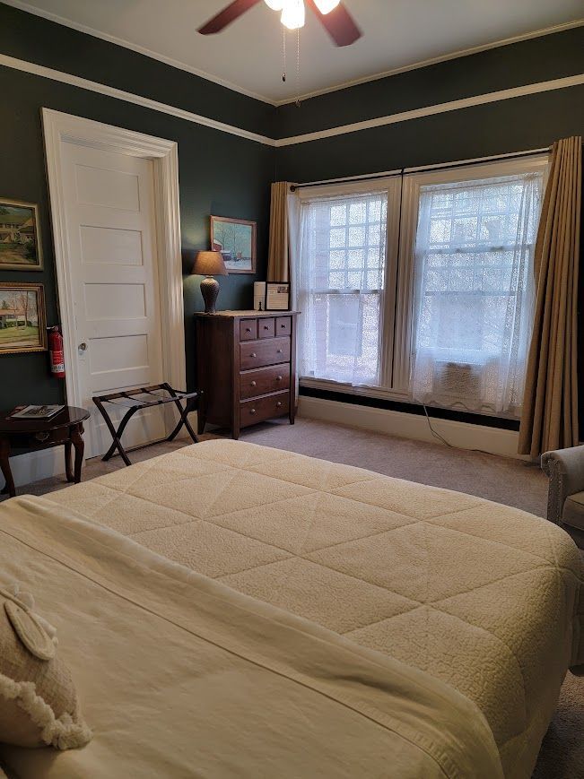 Bedroom with dark green walls, white trim, and a bed. Includes dresser, windows with curtains.