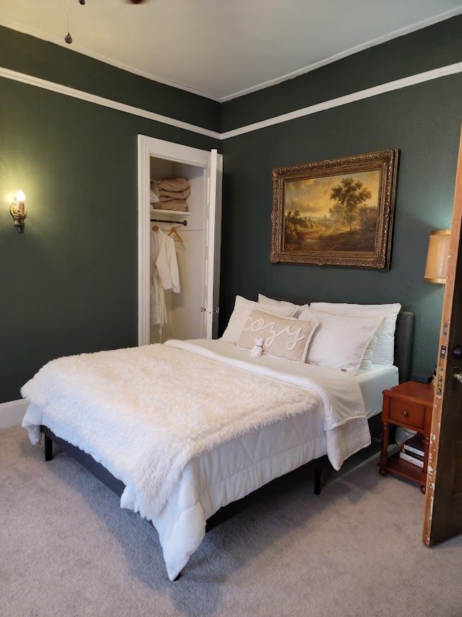 Bedroom with a bed, artwork, and open closet against dark green walls and white trim.