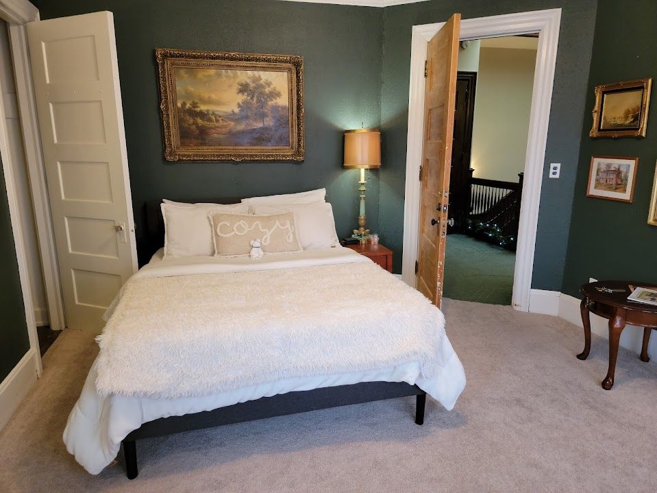 Bedroom with dark green walls, bed, open doorway, and artwork.