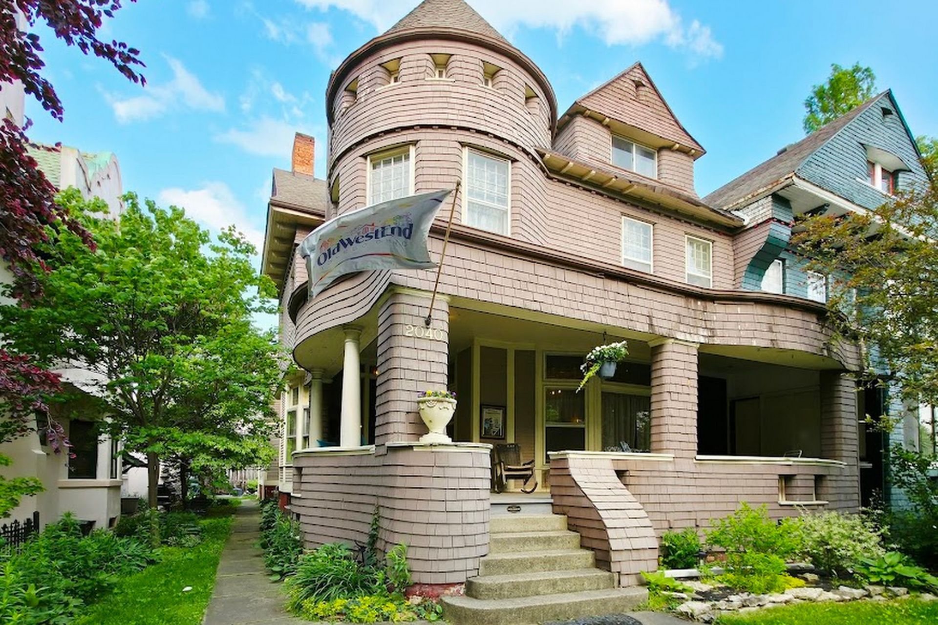 Pink brick Victorian house with turret, porch, and steps on a sunny day.