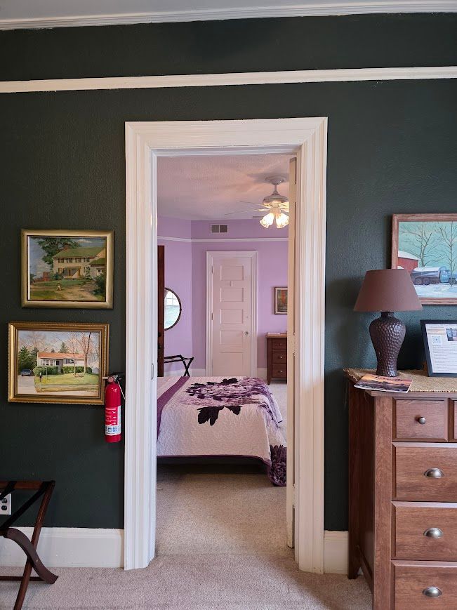 Dark green doorway leading to a light purple bedroom with a bed and a dresser.