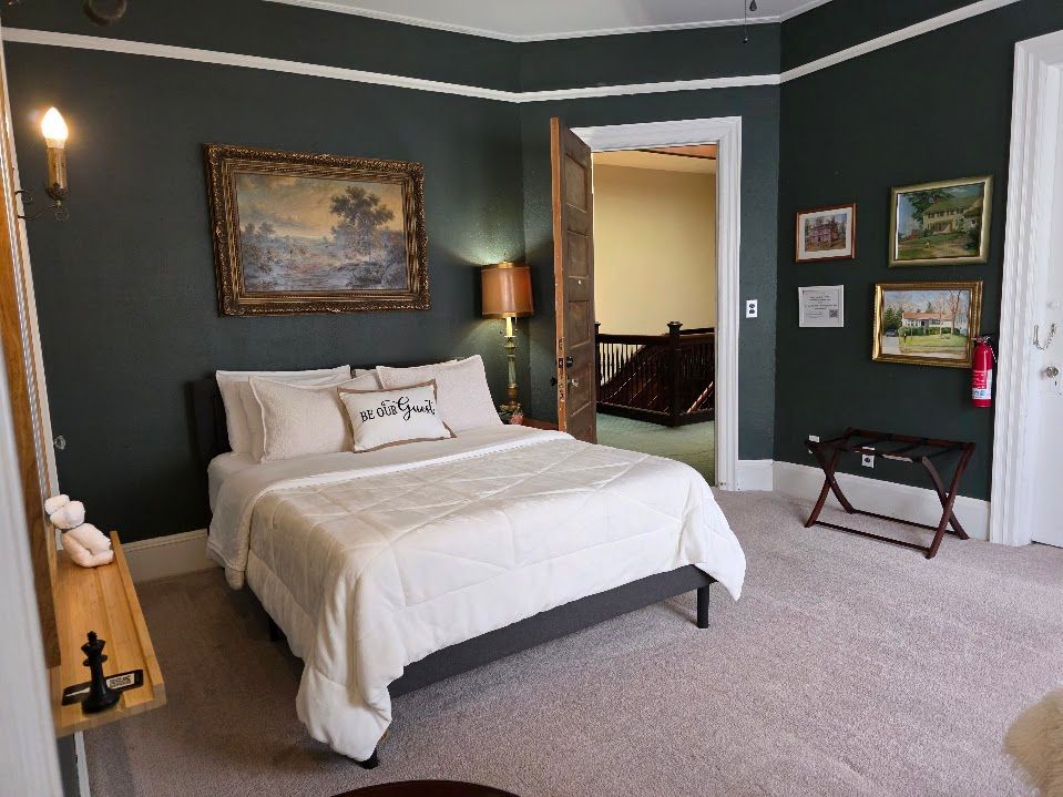 Bedroom with dark green walls, bed, artwork, and open doorway.