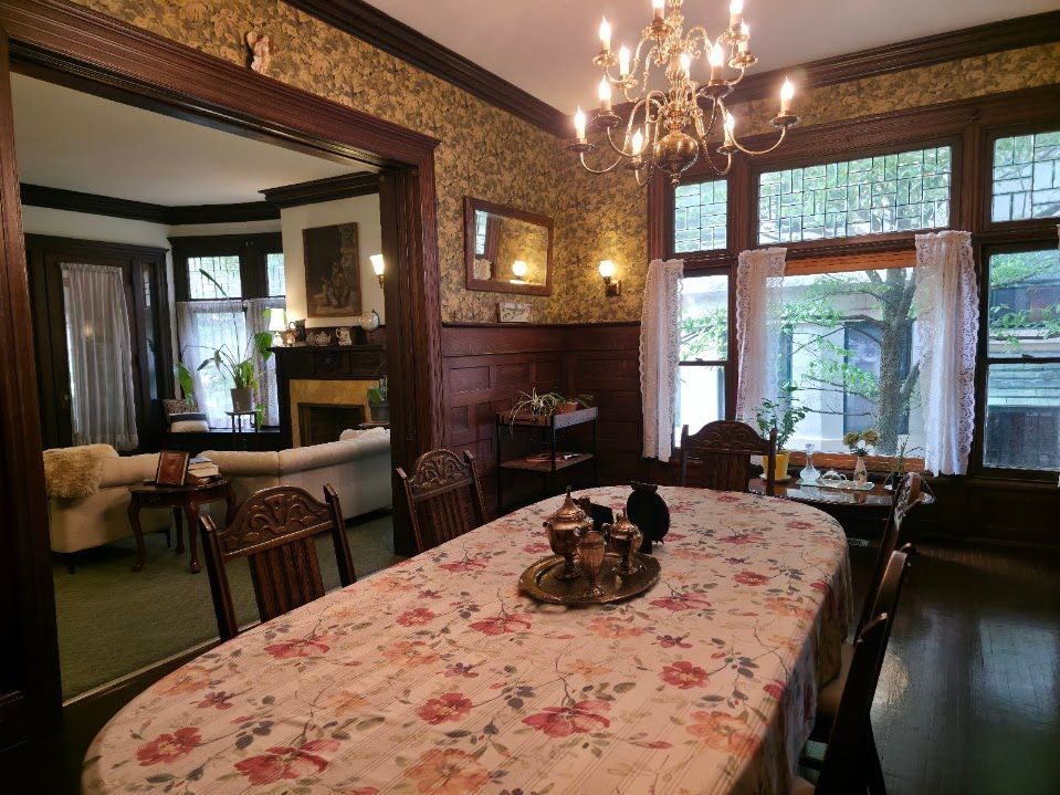 Formal dining room with long table set for a meal, doorway to a living room, and large windows.