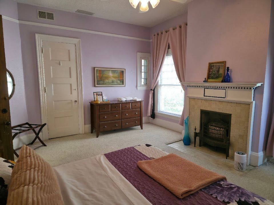 Bedroom with lavender walls, fireplace, and double bed.