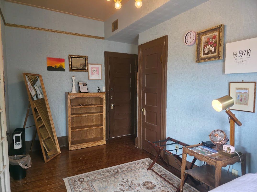 Bedroom with blue walls, wood furniture, rug, artwork, and an open doorway.
