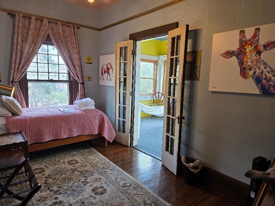 Bedroom with bed, patterned rug, open doors to another room, giraffe art.