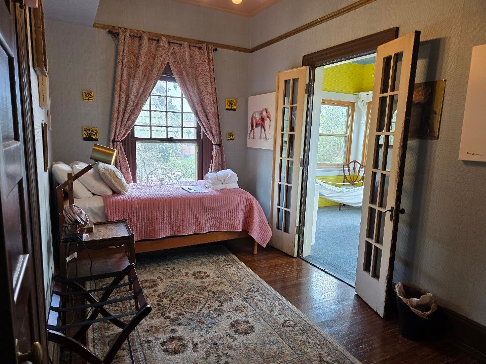 Bedroom with pink curtains, bed, and open French doors leading to a sunroom.