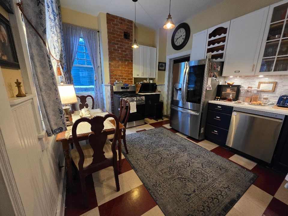 Kitchen with checkered floor, rug, dining table, stove, brick wall, and stainless steel appliances.