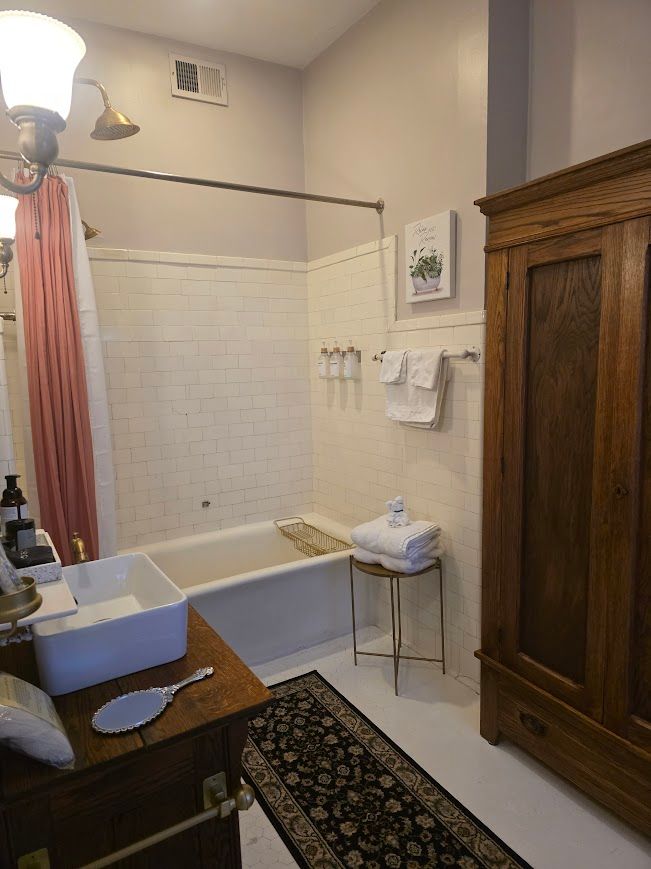 Bathroom with a tub and shower, white tile, a dark wooden cabinet, and a pink shower curtain.