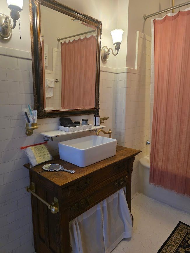Bathroom with antique wooden vanity, white vessel sink, and pink shower curtain.