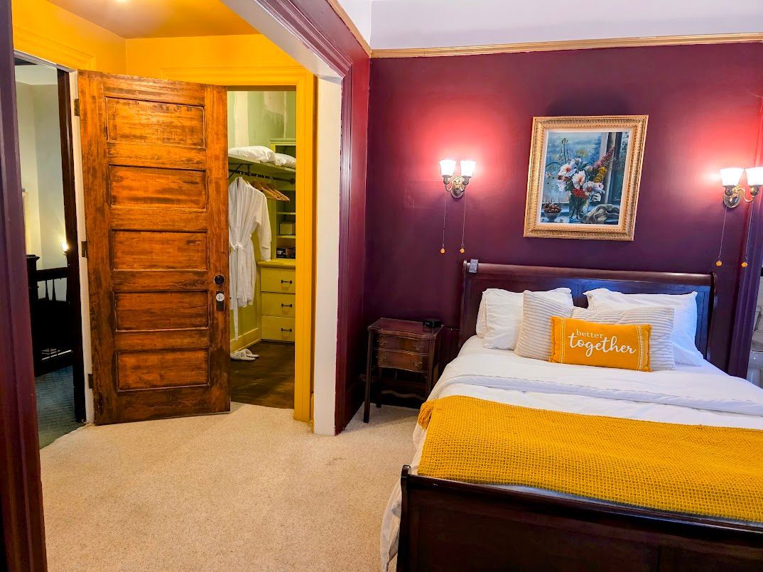 Bedroom with purple walls, wooden bed, and open closet; doorway to a yellow-painted room.