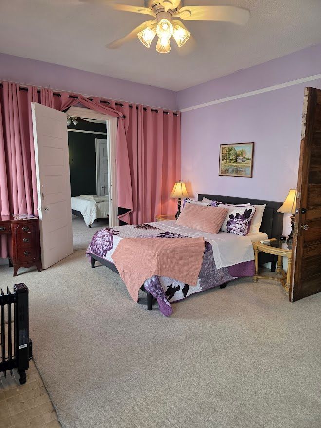 Bedroom with a double bed, pink curtains, purple walls, and doorway to another room.