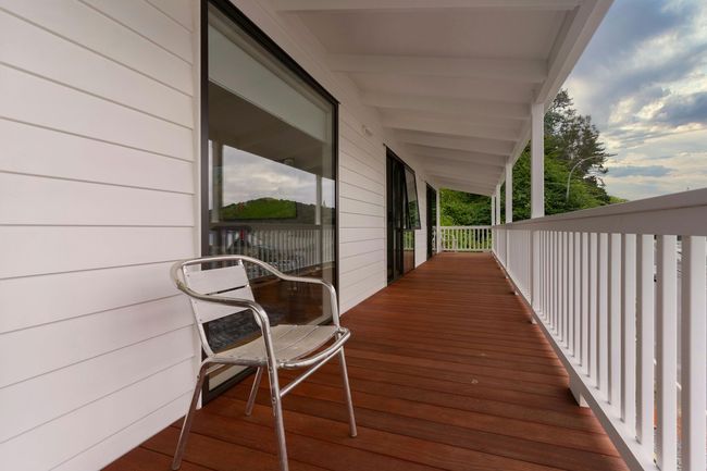 Covered wooden porch with white railing and a metal chair beside a house.
