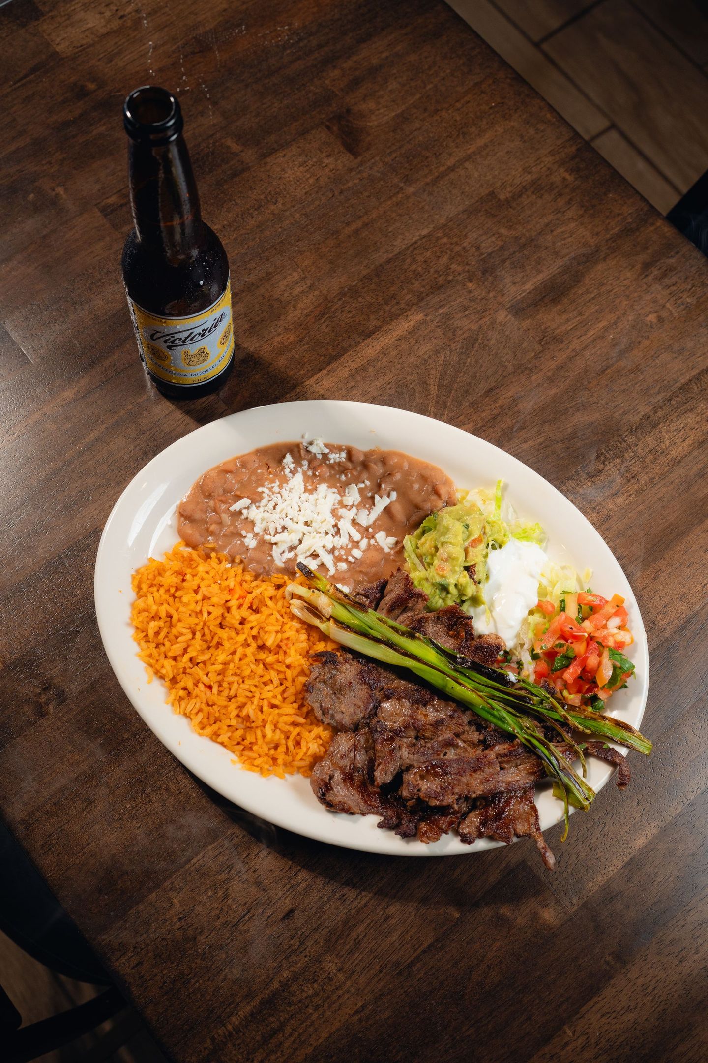 A plate of food and a bottle of beer on a wooden table.