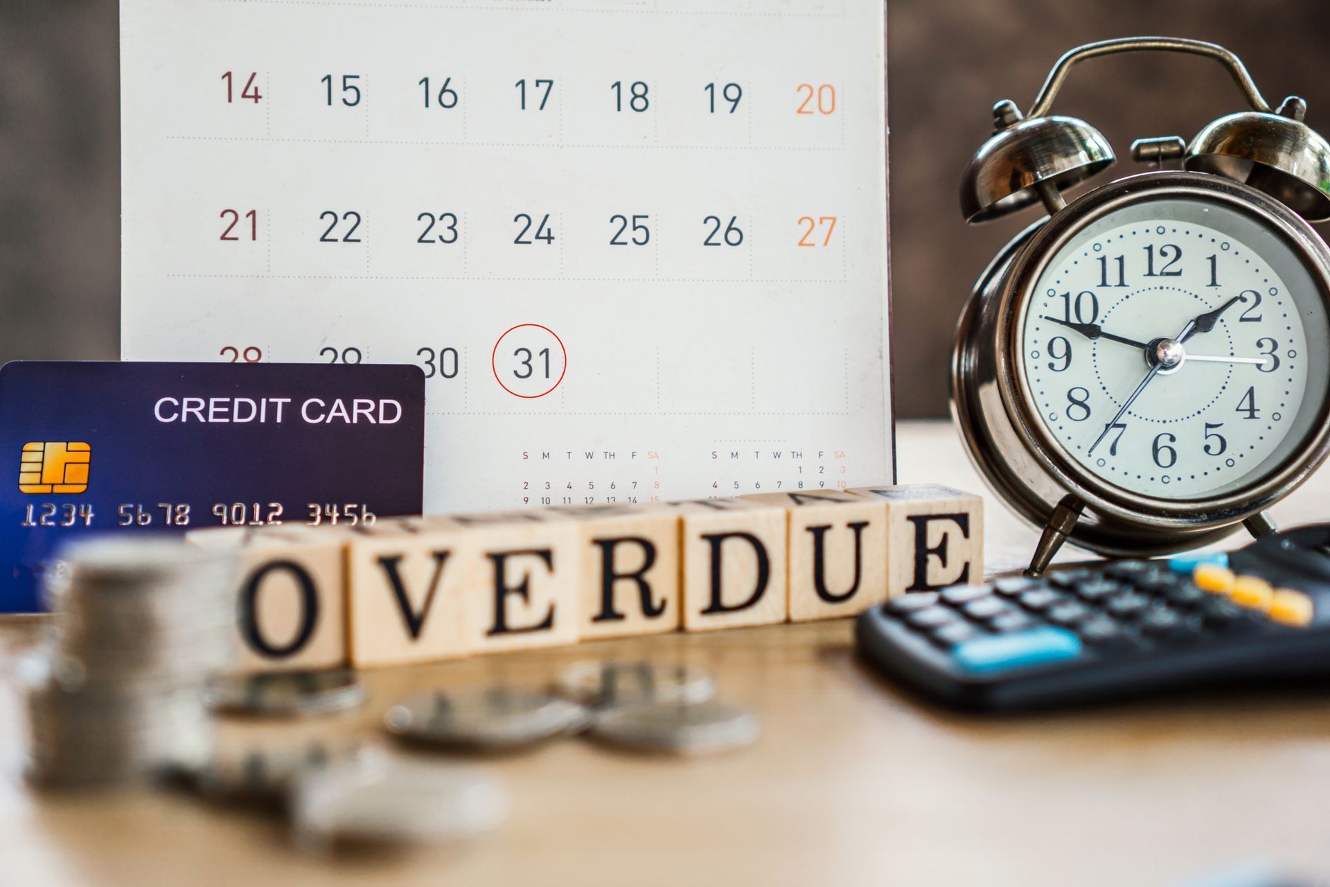 A credit card , an alarm clock , a calculator , and a calendar are on a table.
