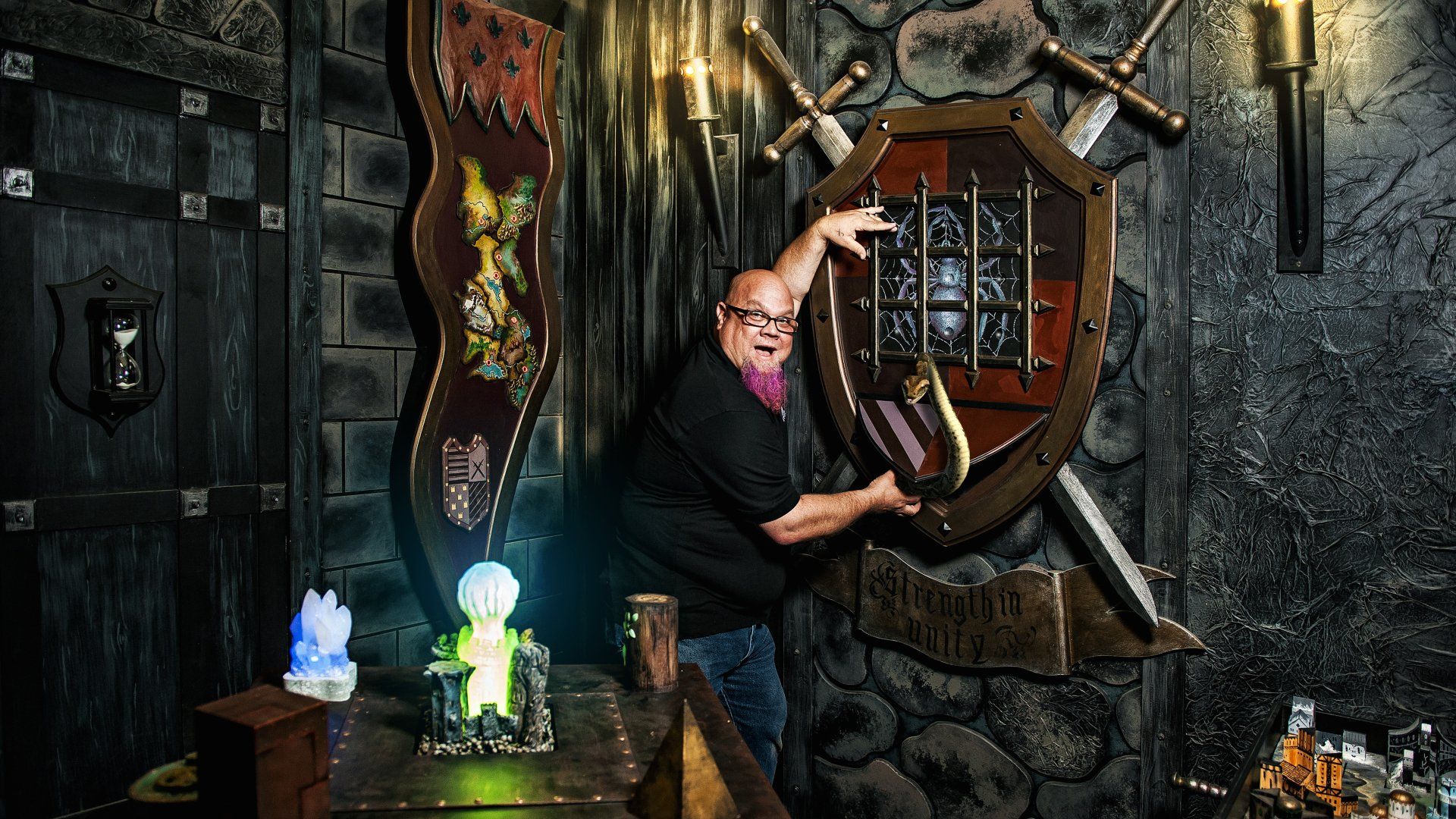 Man interacting with a medieval-themed escape room puzzle, reaching towards a shield with swords on a stone wall.