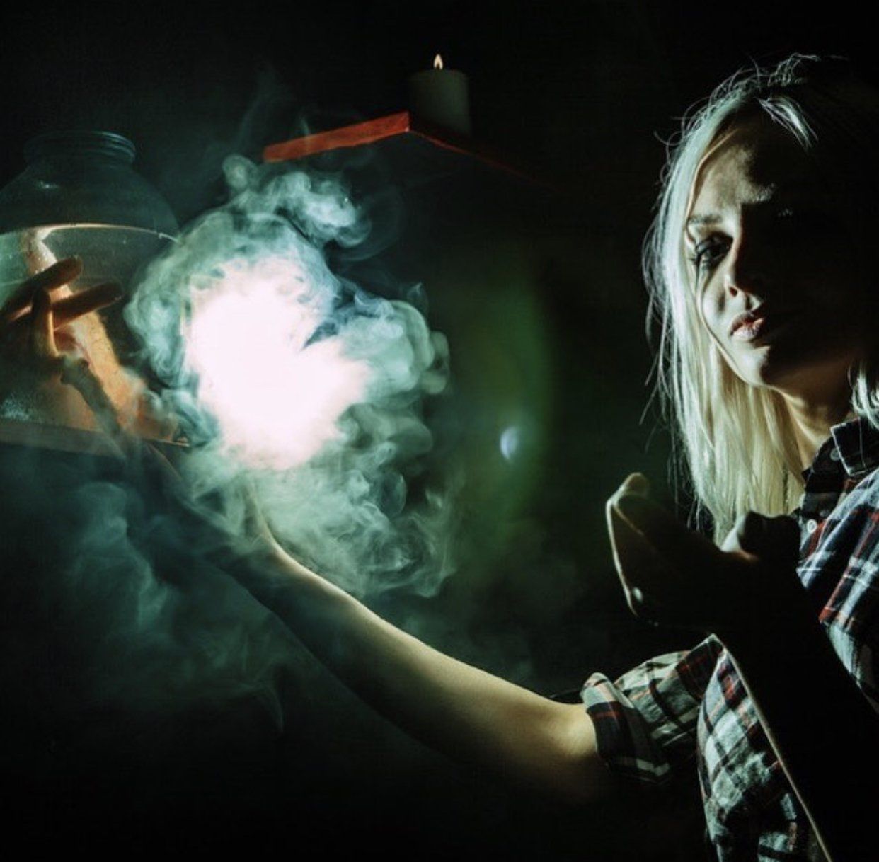 Blonde woman casts a spell, holding a glowing orb, surrounded by smoke in a dimly lit room.