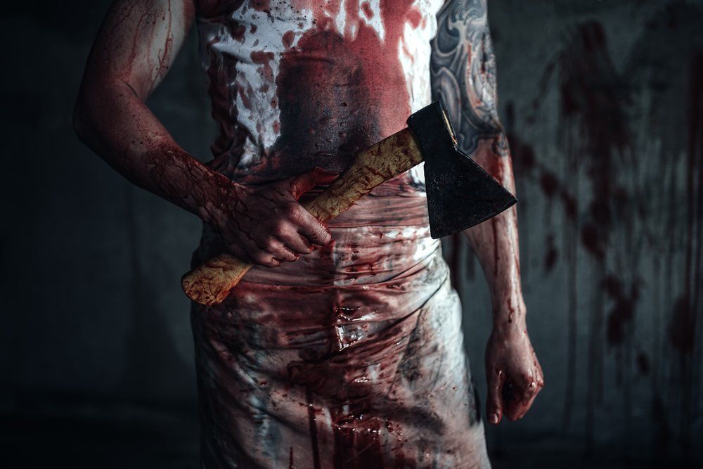 Person covered in blood holding an axe in a dimly lit room.