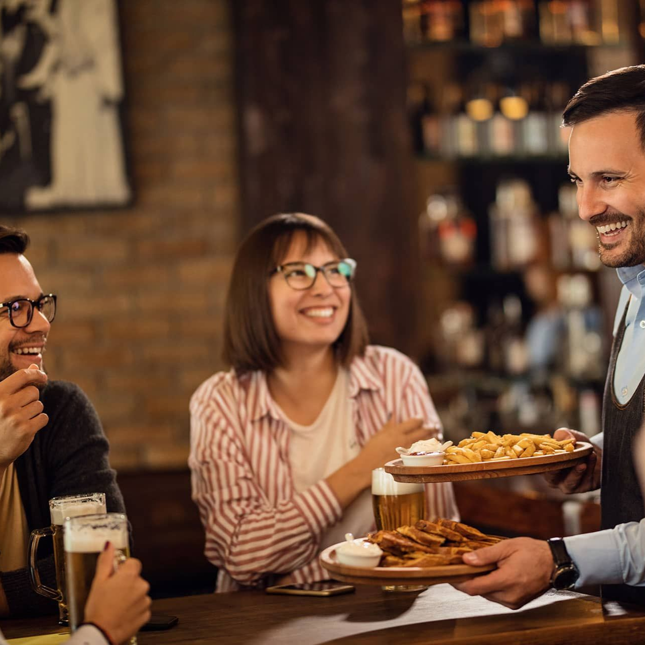 A server smiles while placing plates of food in front of customers at a bar.