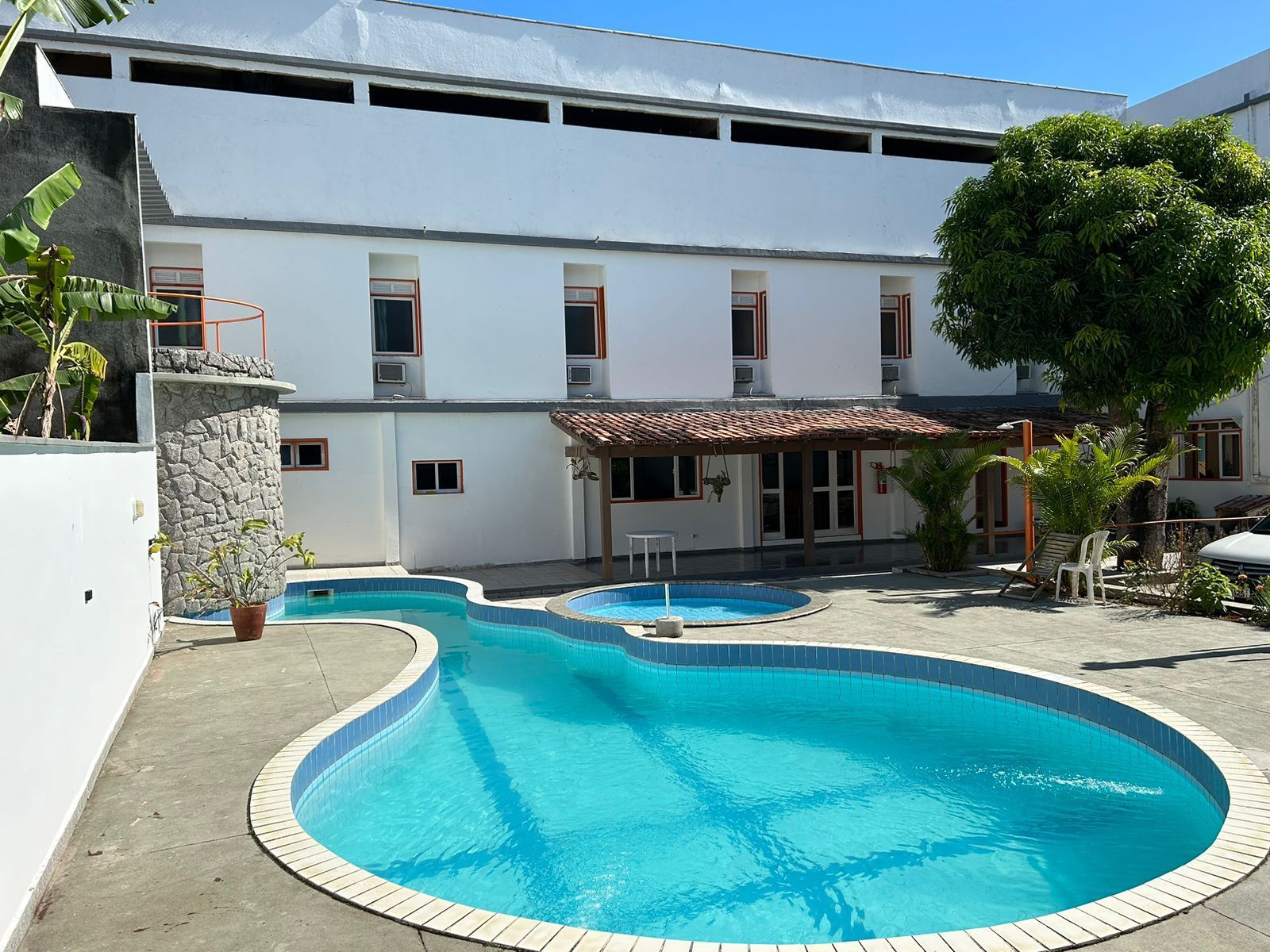 Um prédio branco de três andares com uma piscina azul na frente.Pousada Itaúna 