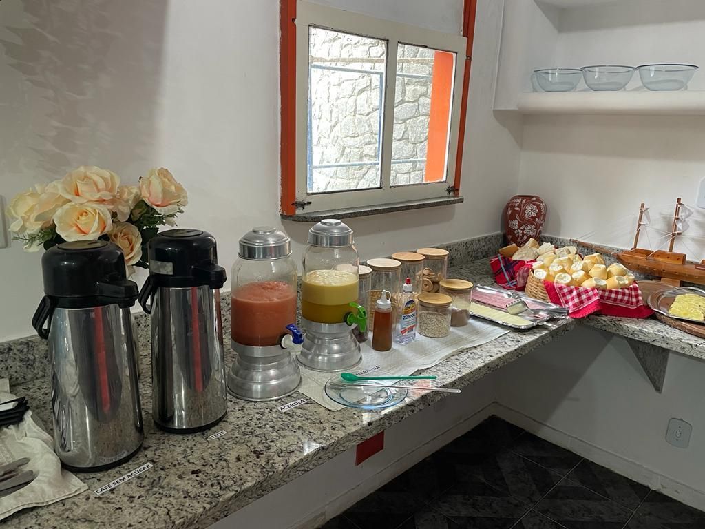 Buffet de café da manhã com café, suco, doces e pães em uma bancada de granito.Pousada Itaúna 