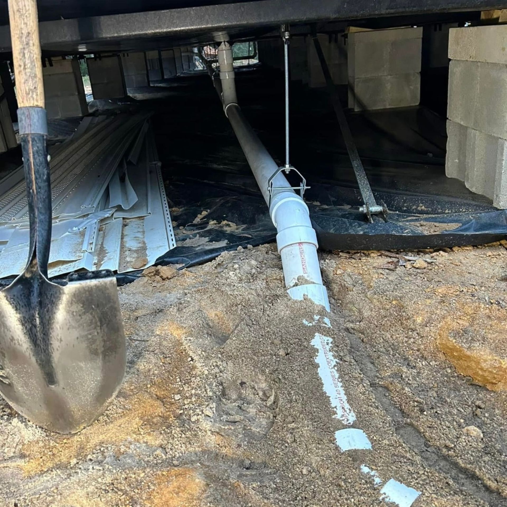Black River Plumbing & Gas LLC - Shovel next to exposed plumbing under a building, resting on dirt.