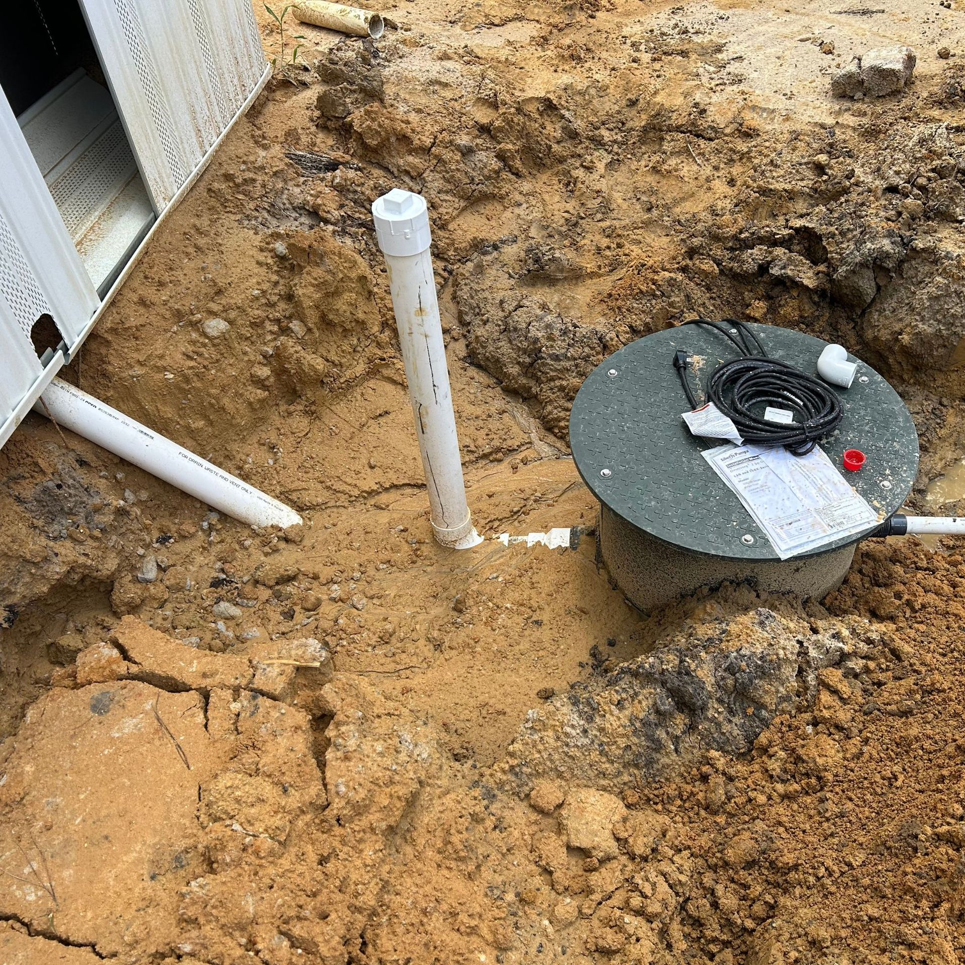 Black River Plumbing & Gas LLC -Construction site: Septic tank installation with pipes and wiring visible in brown soil.