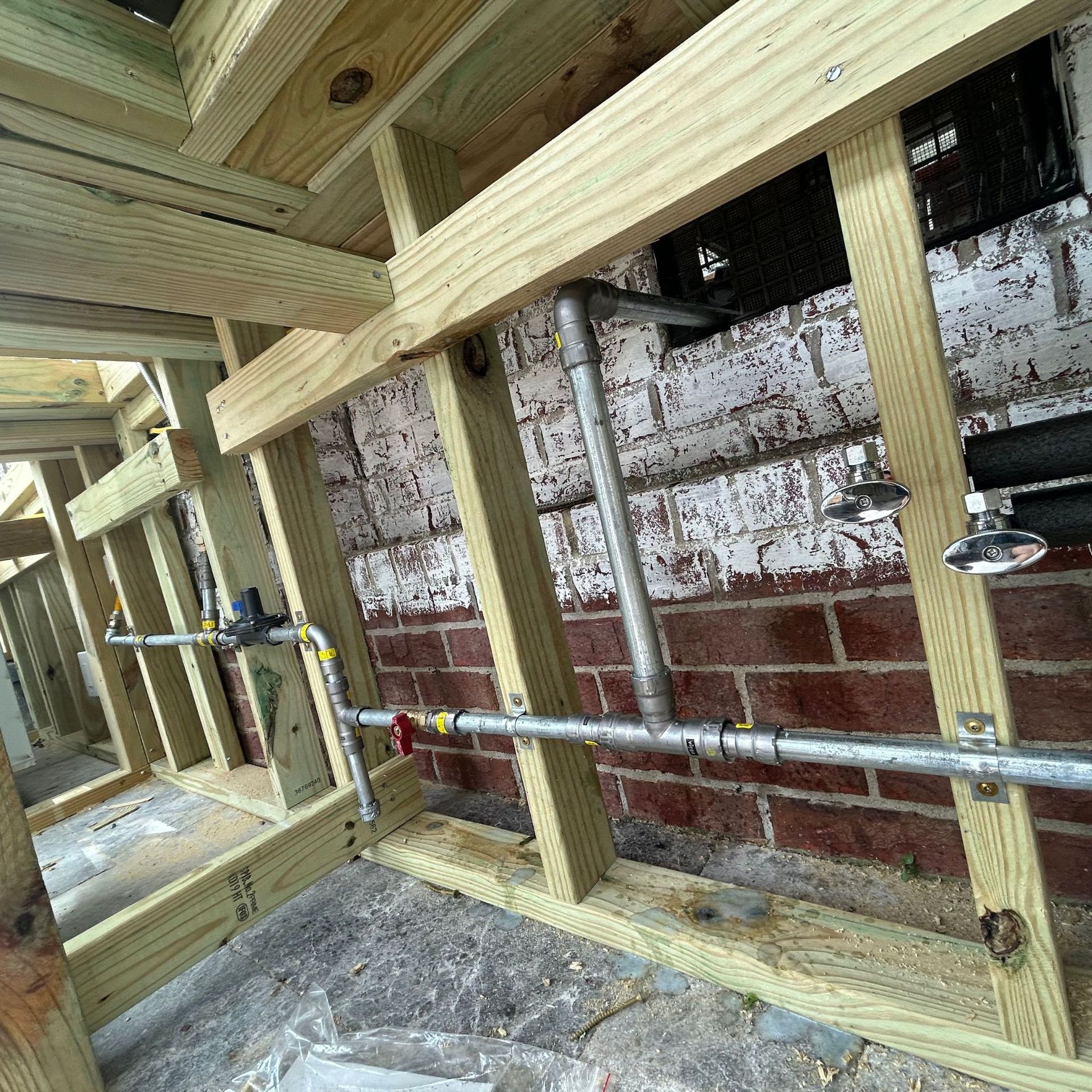 Black River Plumbing & Gas LLC -Framed wood structure with plumbing pipes and fixtures against a brick wall.