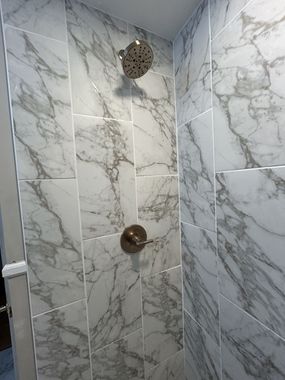 Shower with marble-like tile, bronze fixtures, and a large showerhead.