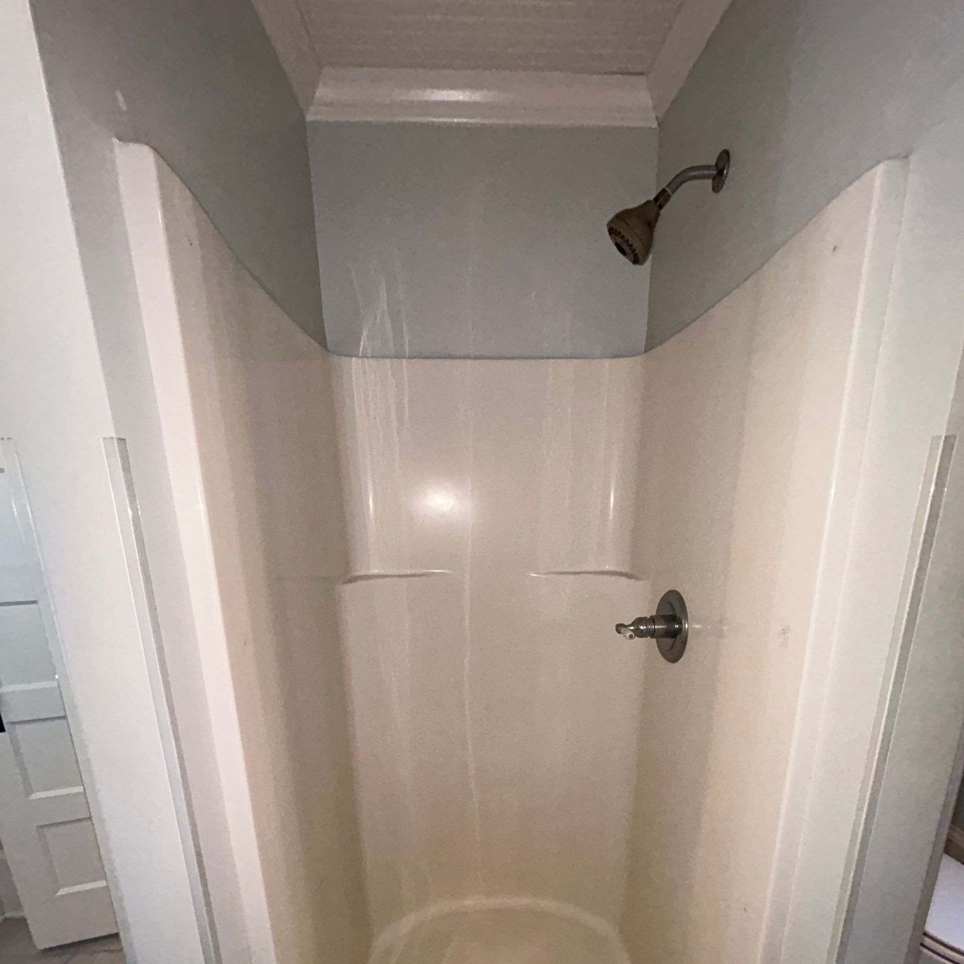 A small, off-white shower stall with bronze showerhead and chrome fixtures, against light blue walls.