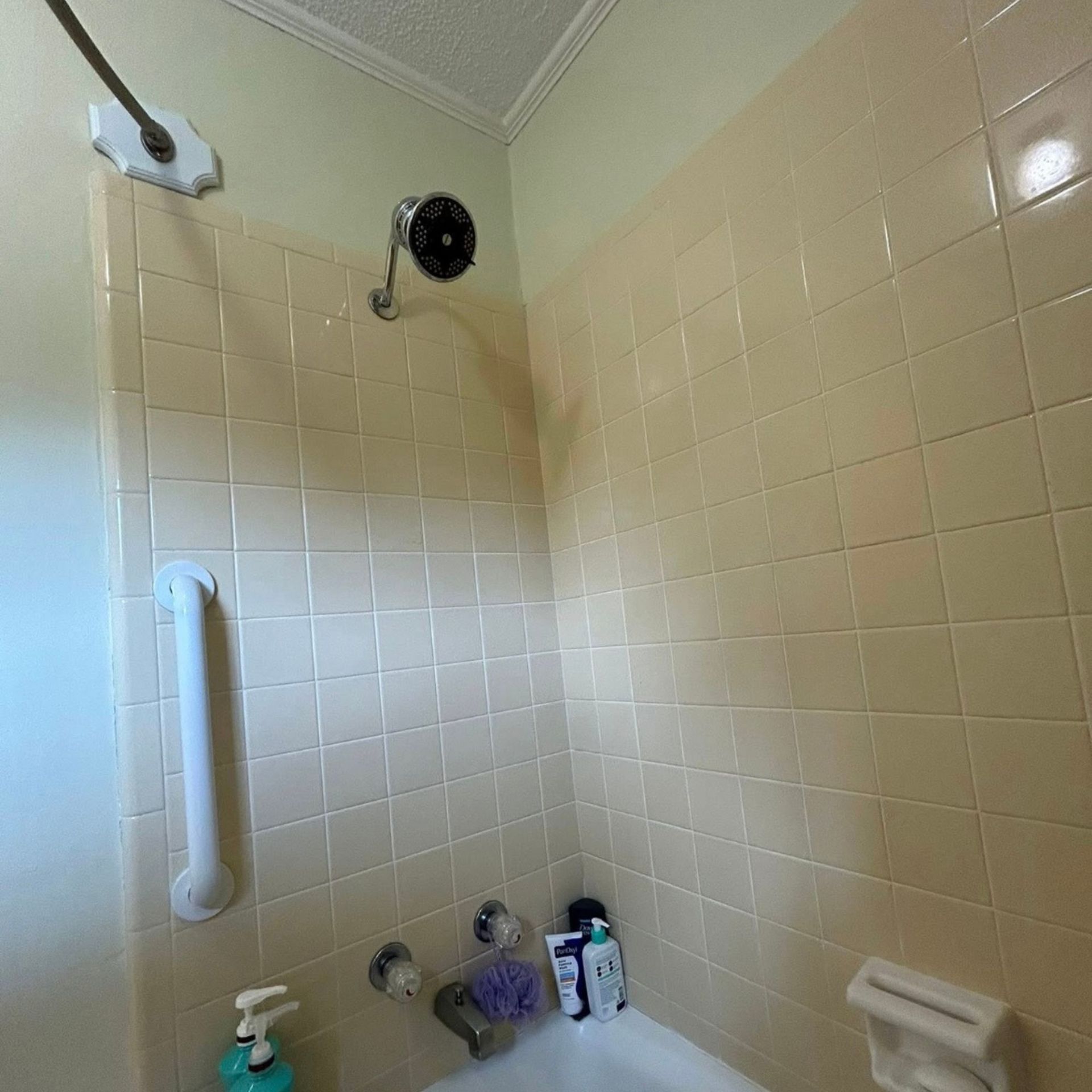 Black River Plumbing & Gas LLC -Shower with beige tiles, showerhead, grab bar, and soap bottles.