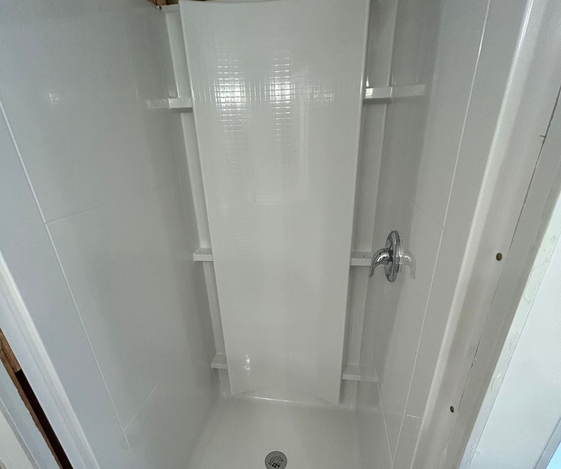 White shower stall with built-in shelves, a center panel with small white tiles, and a chrome showerhead.