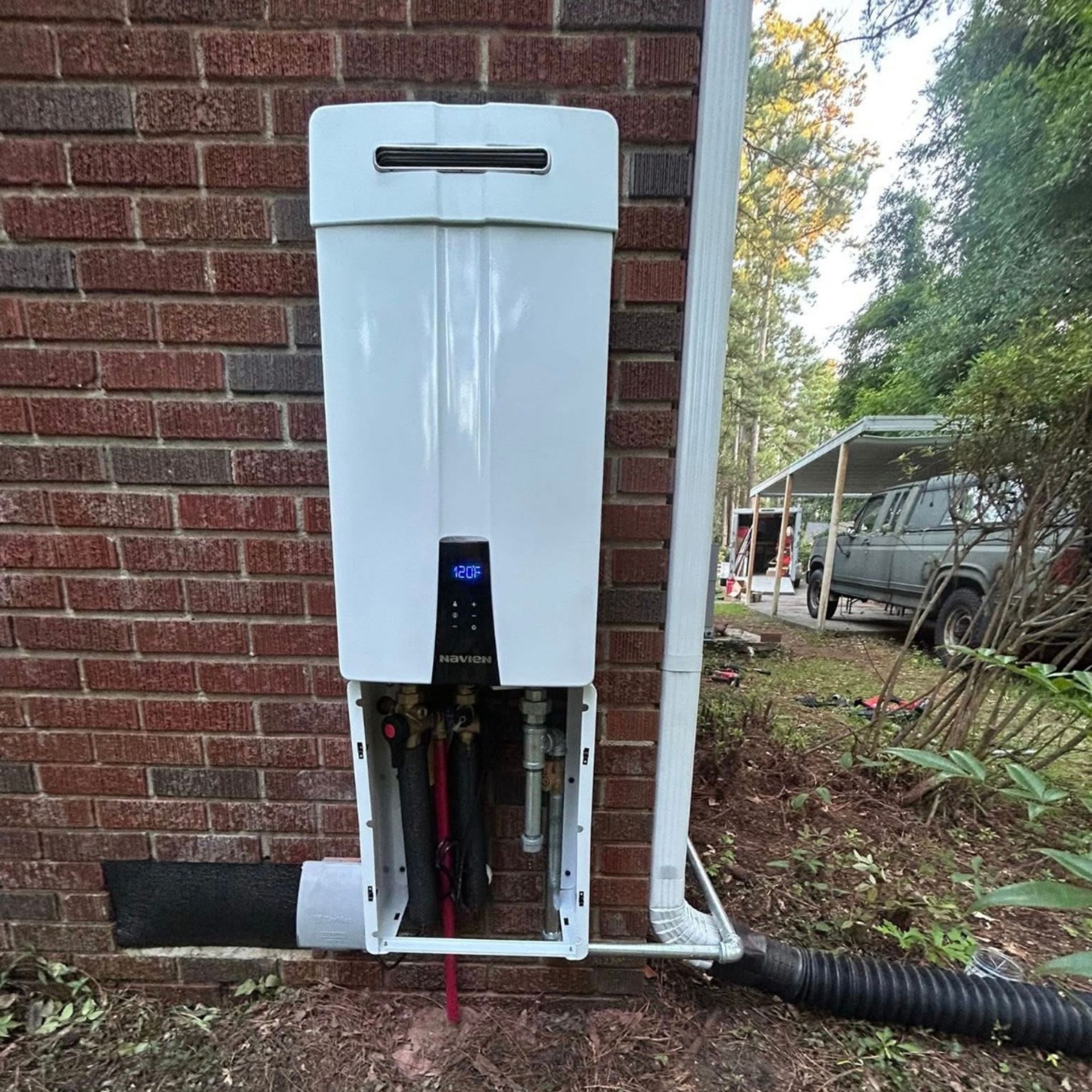 White water heater unit mounted on brick wall, next to a downspout.