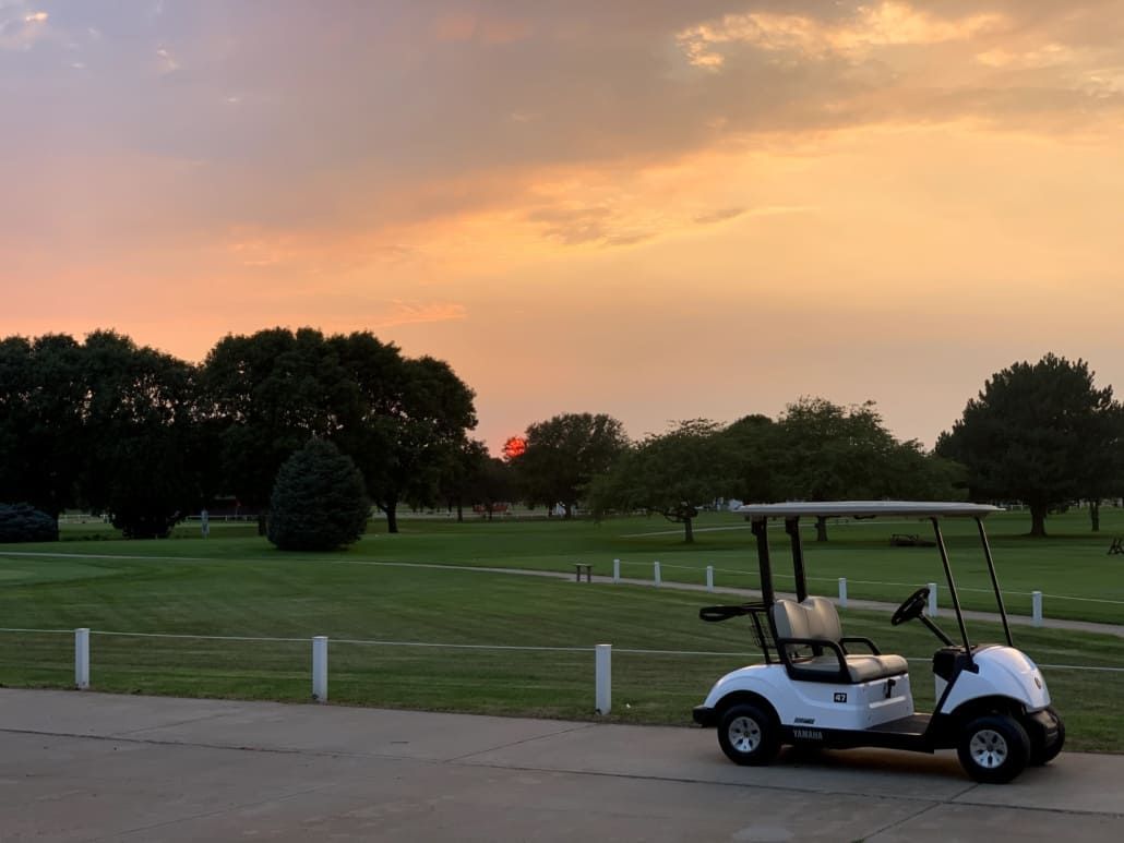 A golf cart is parked in front of a golf course at sunset.