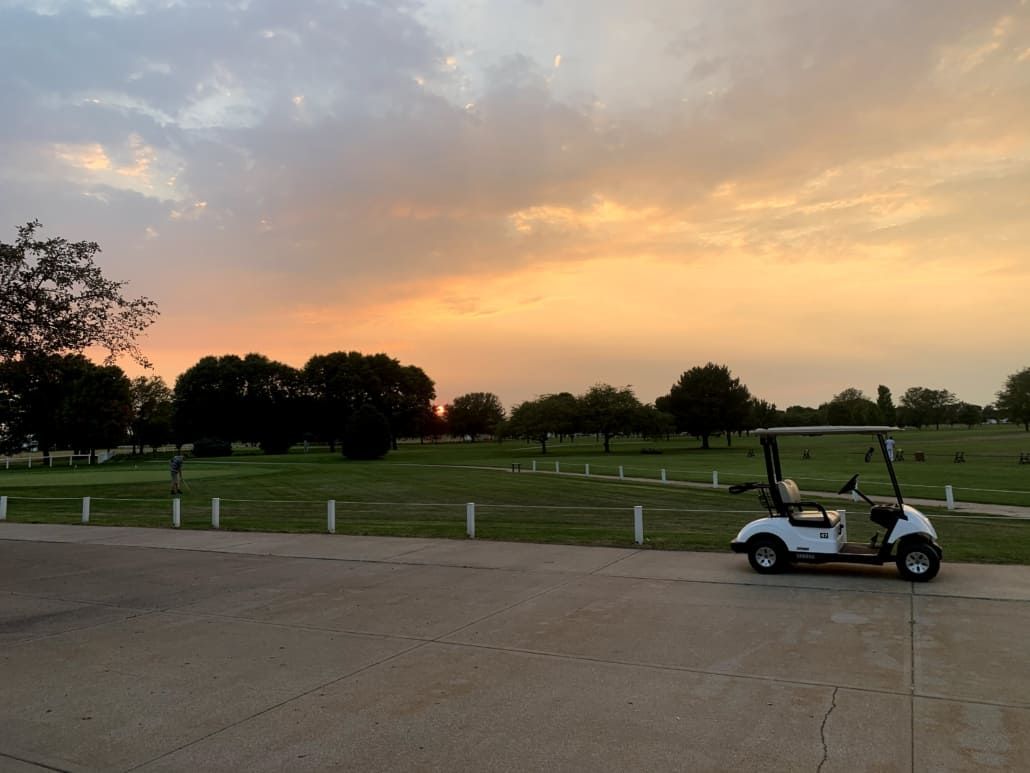 A golf cart is parked in front of a golf course at sunset.