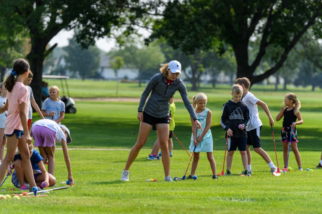 A woman is teaching a group of young girls how to play golf.