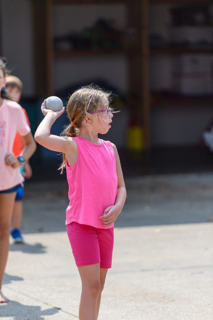 A little girl in a pink shirt is throwing a ball.