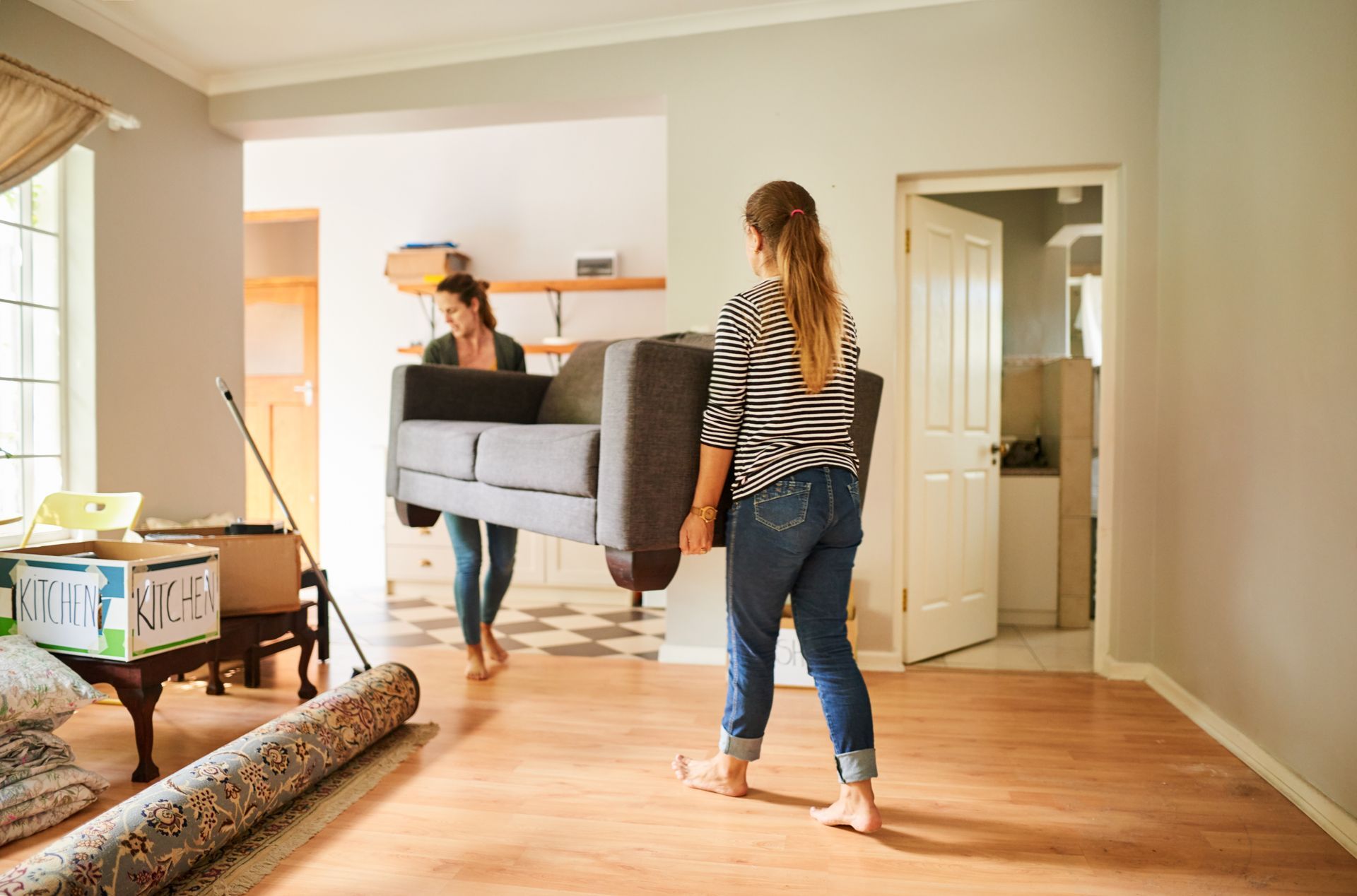 Two women are carrying a couch into a new home.
