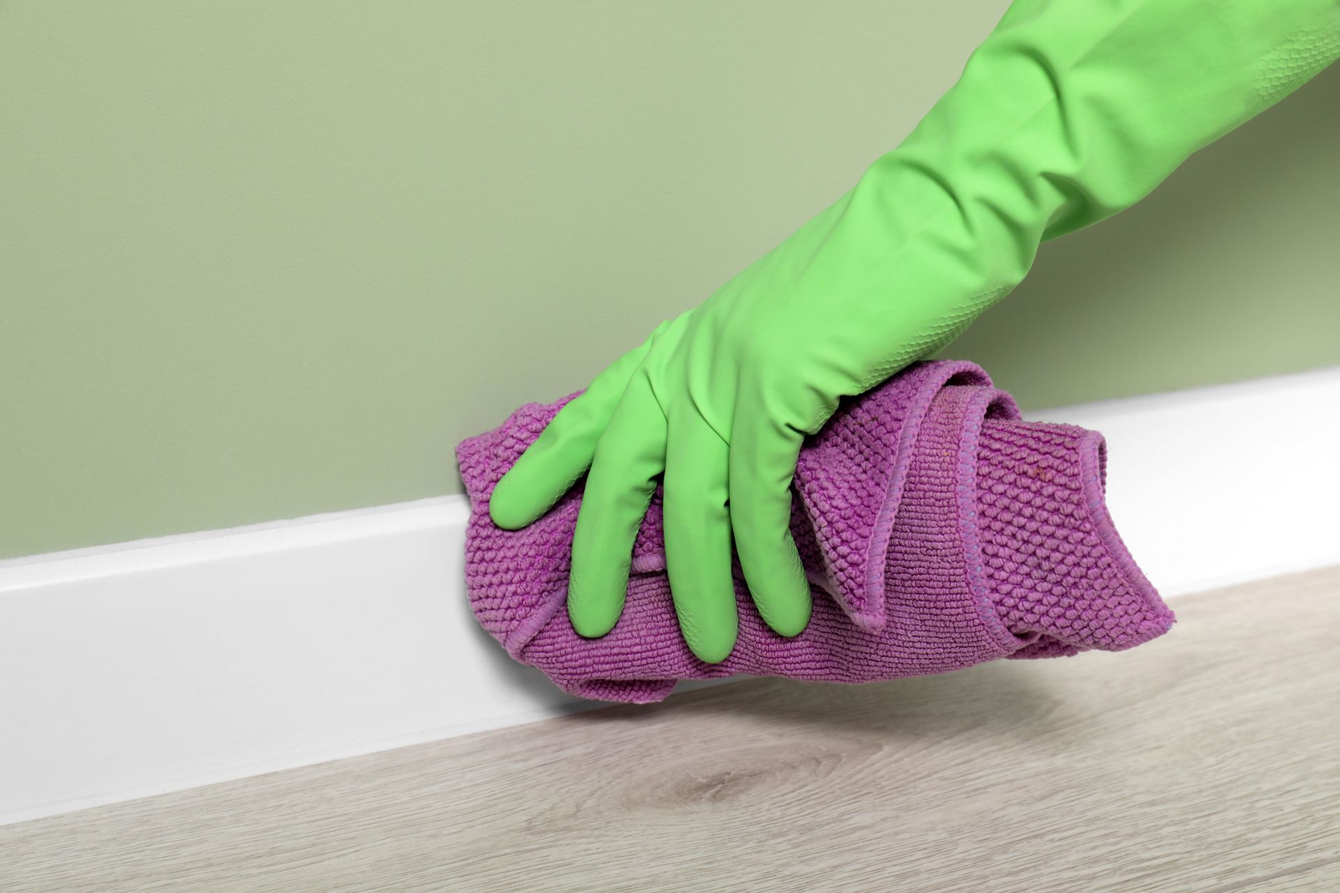 A person wearing green gloves is cleaning the floor with a purple cloth.