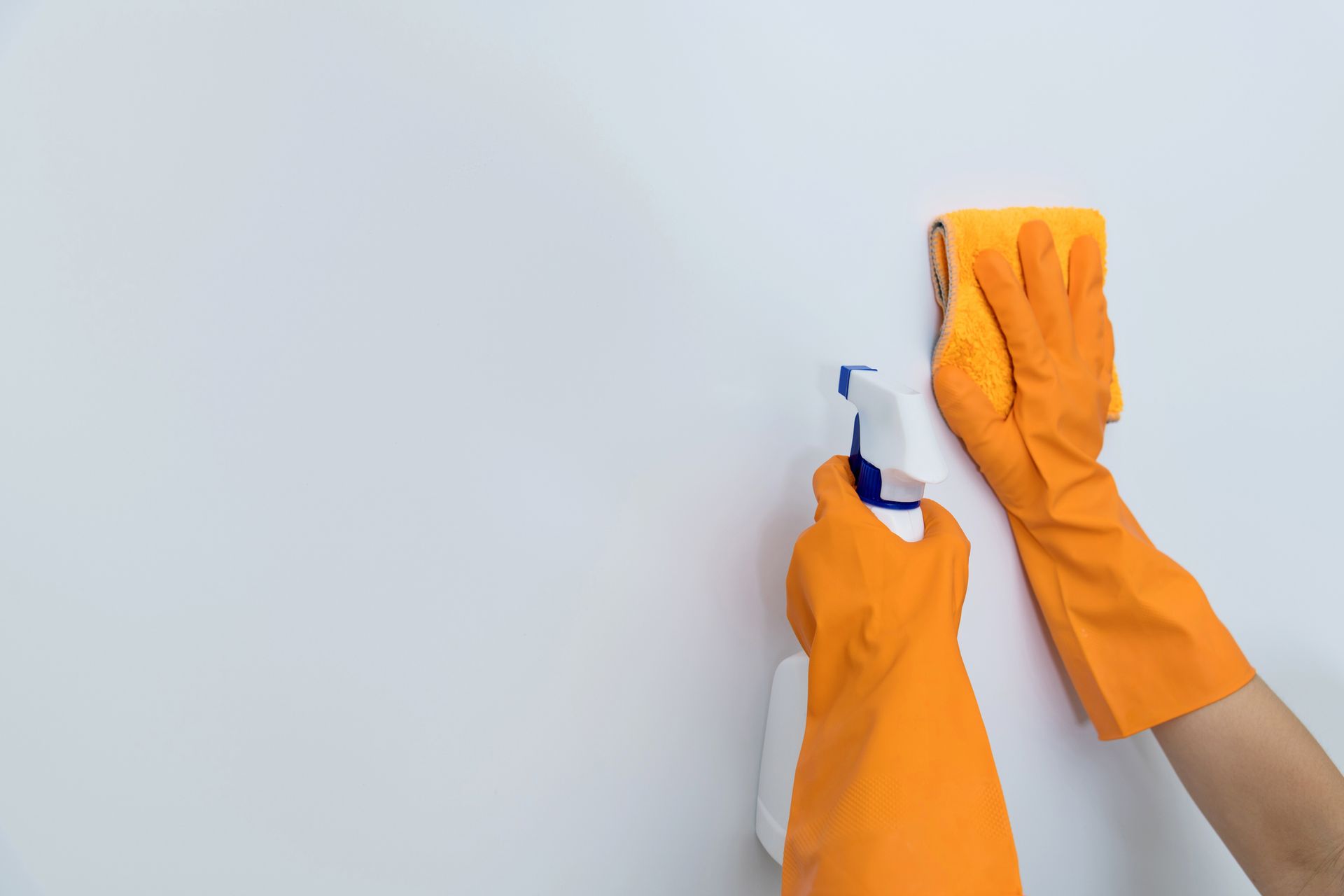 A person wearing orange gloves is cleaning a wall with a spray bottle and a sponge.