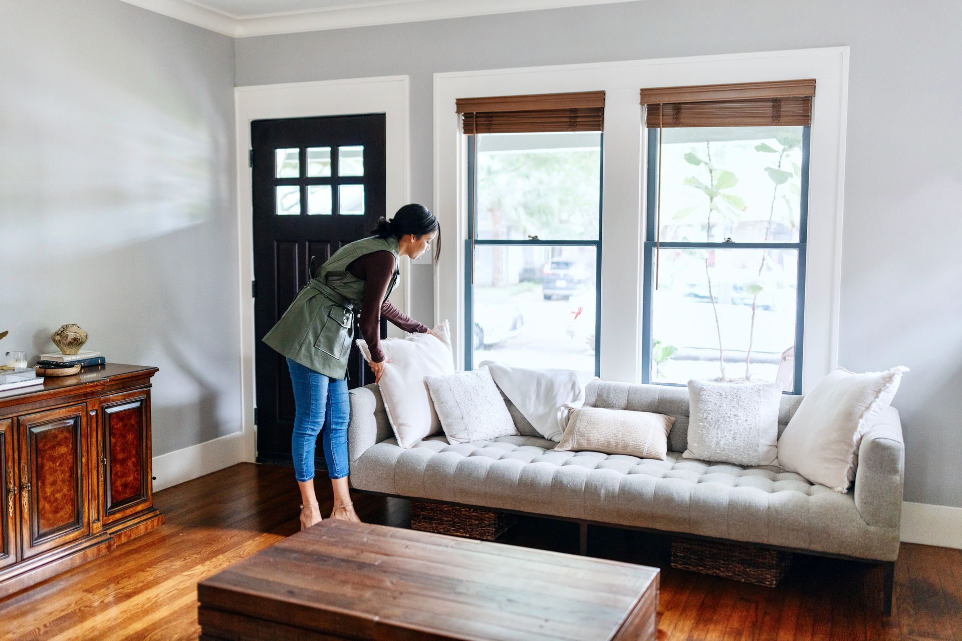 A woman is putting pillows on a couch in a living room.