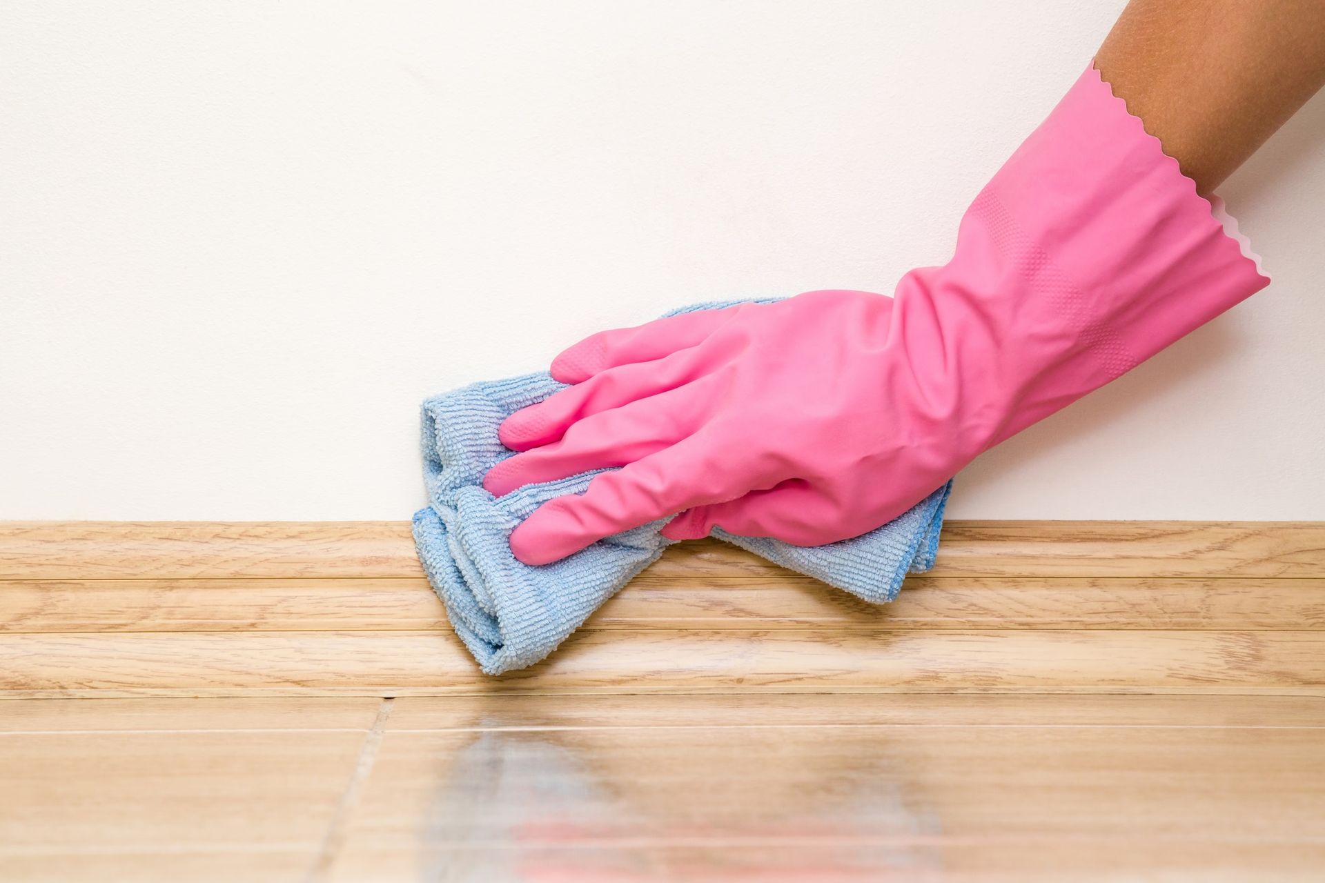 A person wearing pink gloves is cleaning a wooden floor with a towel.