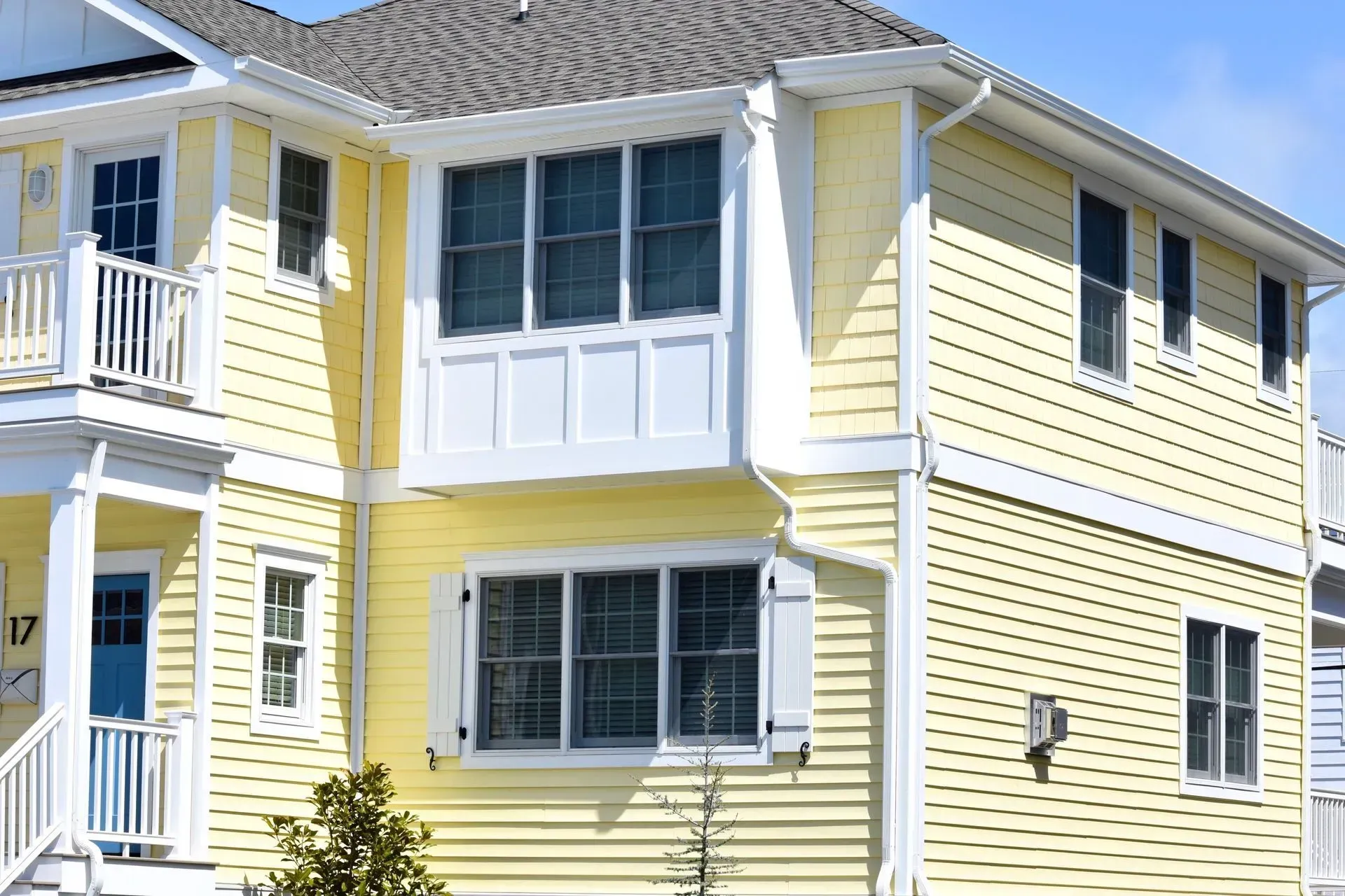 Yellow two-story house with white trim, windows, and balcony against a blue sky.