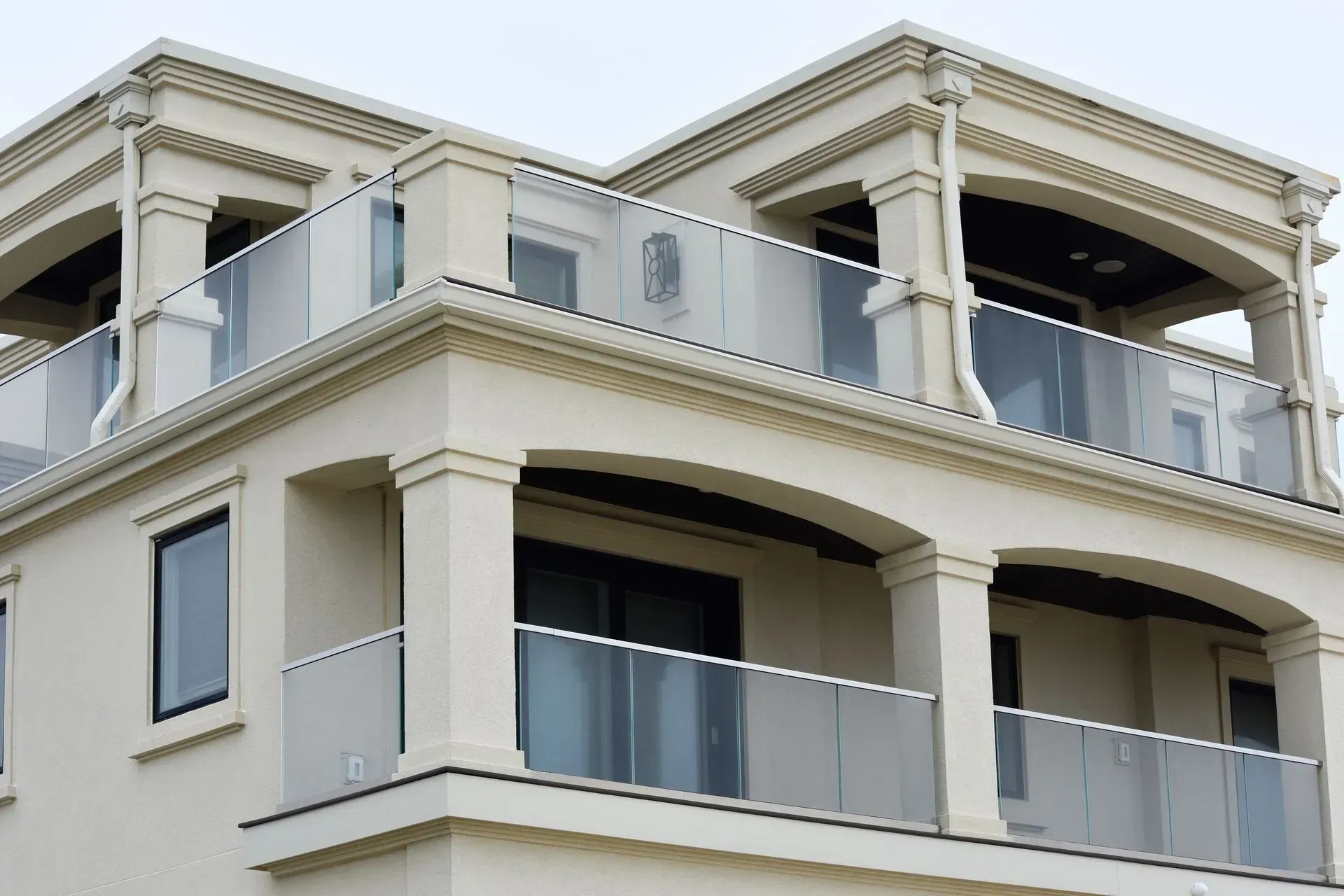 Multi-story building with cream-colored stucco, balconies with glass railings, and ornate architectural details.