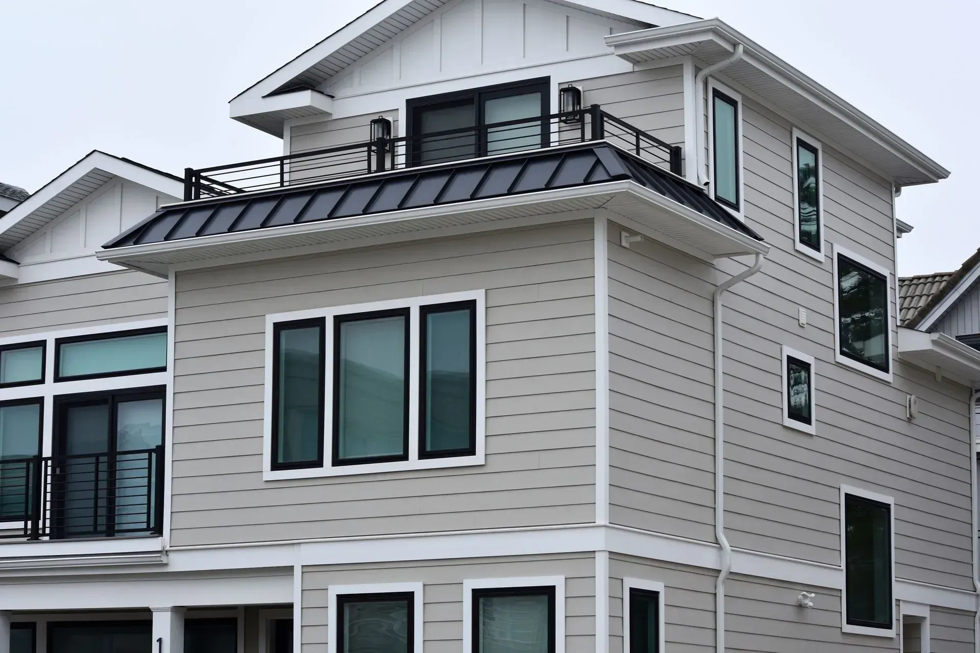 Three-story modern house with light gray siding, black trim, and a rooftop deck with black railings.