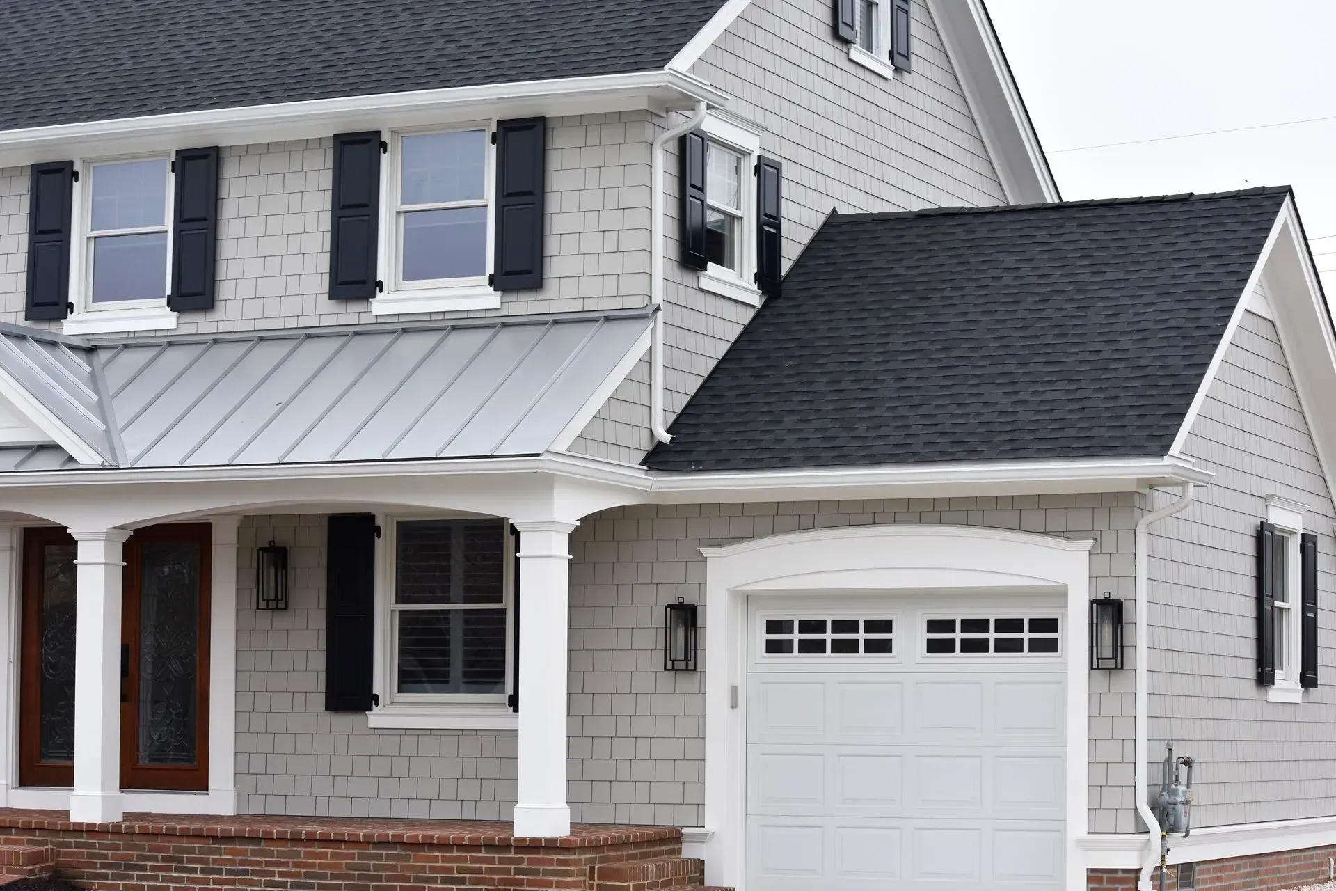 Two-story house with gray siding, black shutters, white trim, and a white garage door.